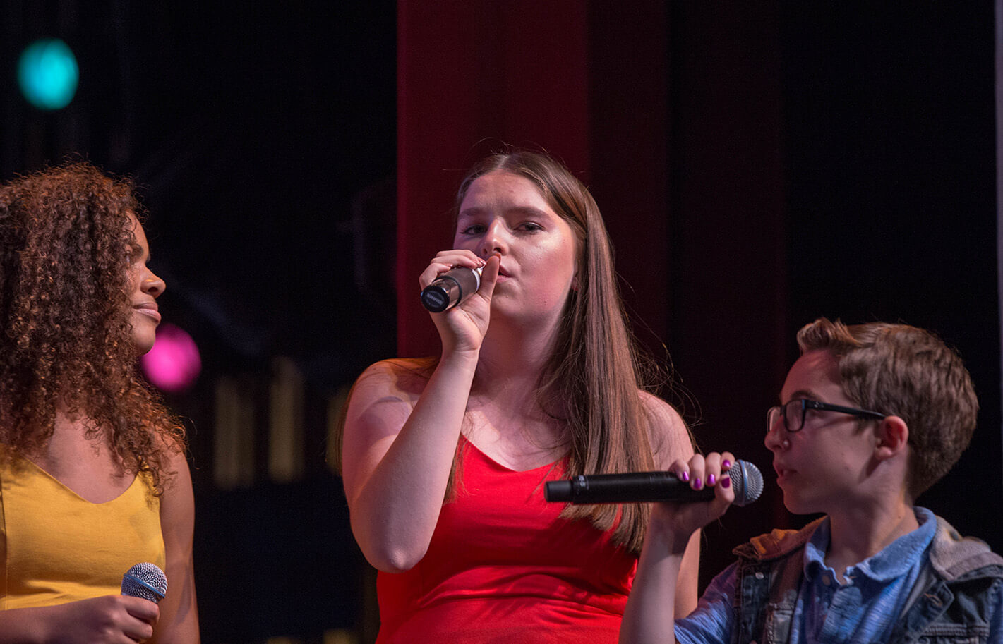 Three people singing on stage with microphones.